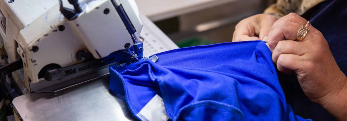 Clemens Uniform crafts a blue work uniform using an industrial sewing machine as part of its commercial uniform program.