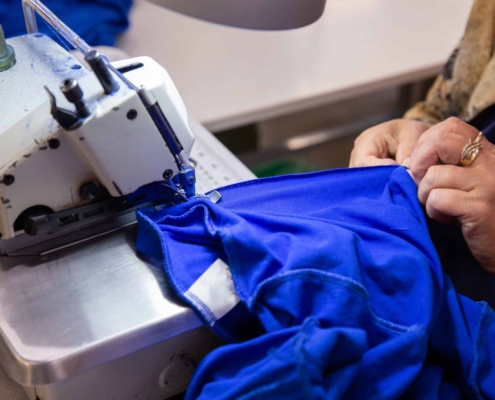 Clemens Uniform crafts a blue work uniform using an industrial sewing machine as part of its commercial uniform program.